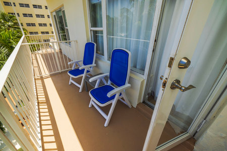 Close-up view of hotel balcony with two blue chairs near open door on sunny day. Miami Beach. USA.の写真素材