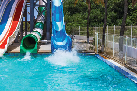 Colorful water slides with strong splash in pool at tropical amusement park on hot sunny summer day. Curacao.の写真素材
