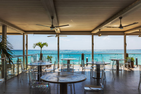 Open terrace restaurant with empty transparent chairs and round tables facing turquoise Caribbean Sea.の写真素材