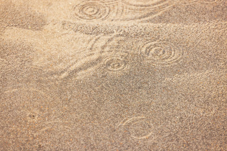 Circular ripples on rough sand during summer rain shower.
