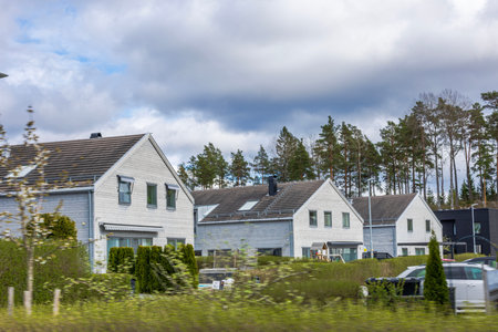 Modern European villas with gray facades and sloped roofs near pine forest under cloudy sky. Sweden.の写真素材