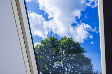 View through attic window showing green tree and white clouds against deep blue summer sky on sunny day. Sweden.の写真素材