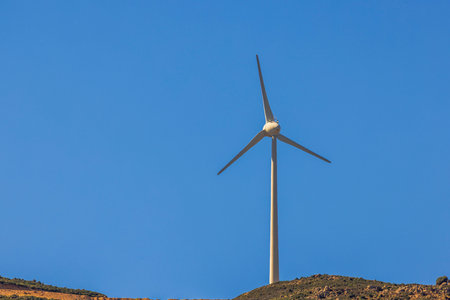 Wind standing turbine on mountain top under clear blue sky generating renewable energy in sunny...