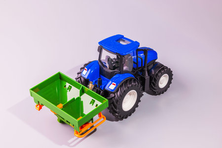 Close up view of RC blue toy tractor with green fertilizer spreader isolated on light background....