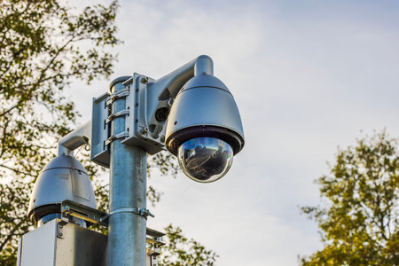 Close-up view of surveillance camera on metal pole with reflection on lens against autumn sky and...