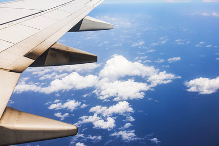Beautiful view of airplane wing above Caribbean Sea with white clouds and ship below. Curacao.