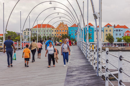 People walking on Queen Emma Bridge with colorful Dutch colonial houses in Willemstad background. Curacao. Willemstad.の写真素材
