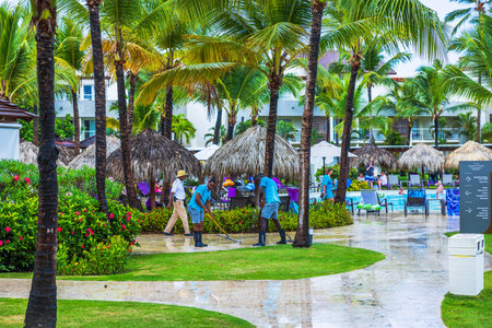 View of Dominican resort workers cleaning wet walkway after rain near swimming pool with tourists. Dominican Republic. Punta Cana.のeditorial素材