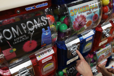 Close up view of child hand using toy capsule vending machine with colorful plastic prizes in store.
