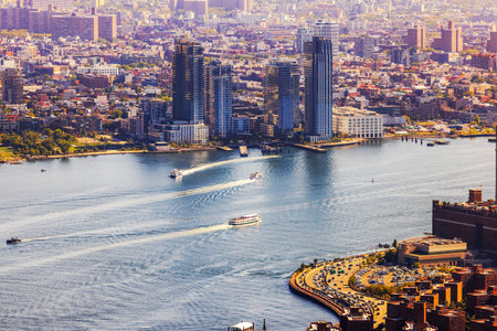 Beautiful aerial view of Manhattan waterfront along East River with boats leaving curved white...