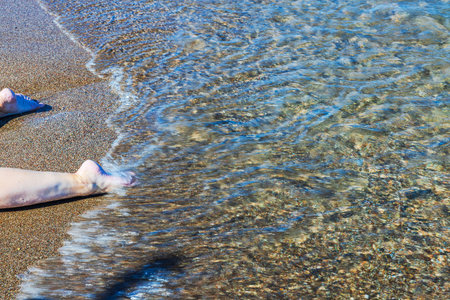 Close up view of feet touching clear water on sandy beach of Aegean Sea. Greece.の写真素材