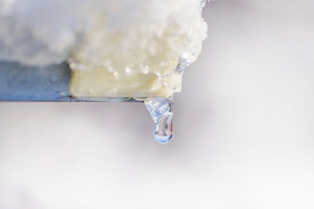 Macro view of melting icicle hanging from metal roof edge in winter. Sweden.