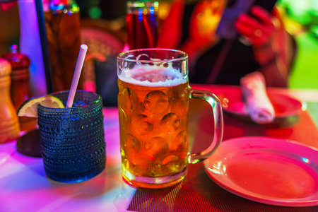 Close up view of cold beer mug on restaurant table glowing colorful evening lights. Miami Beach....