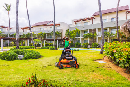 Close up view of gardener mowing green lawn with machine in tropical hotel garden. Dominican Republic. Punta Cana.のeditorial素材