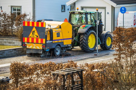 Wide shot of tractor sweeping gravel from residential street in spring municipal cleaning process...