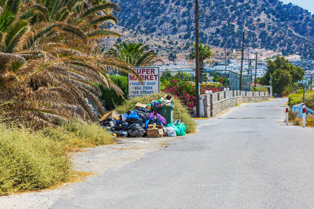 Close up view of coastal road with garbage piles near beach with Aegean Sea and mountains. Kos....
