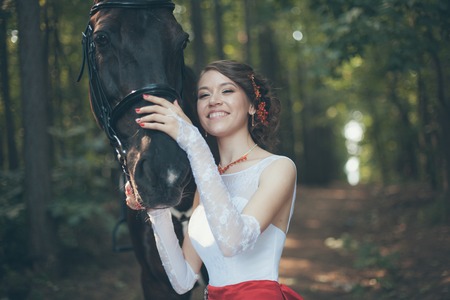 Young woman in white dress standing with horseの写真素材