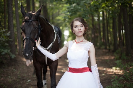 Young woman in white dress standing with horseの写真素材