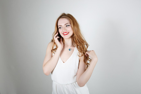 Cute girl with red hair and bright red lipstick on the phoneの写真素材