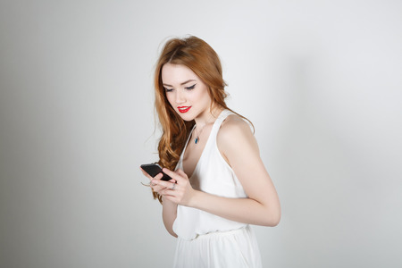 Beautiful girl with red hair and bright red lipstick smiling and looking at the camera on a light background reads smsの写真素材