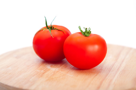 Two tasty red tomatoes on a cutting board on a white backgroundの写真素材