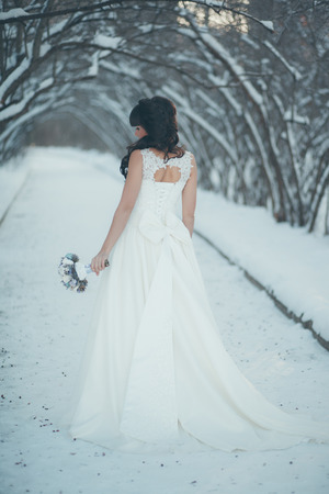 Beautiful bride with a bouquet standing in a snowy winter park at the beautiful snow-covered treesの写真素材
