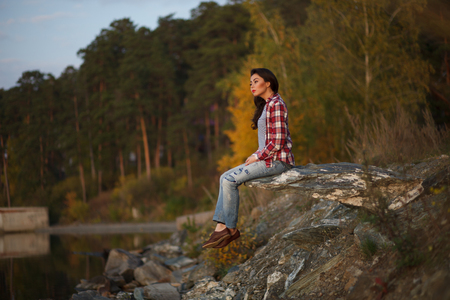 Woman sitting on a sand beach in front of sunset and ocean or lake in autumnの写真素材