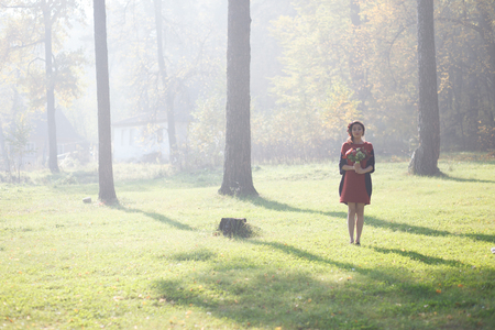 Girl in the image of a forest fairy with flowers in her hands. Sun rays beating down on woman walking in forestの写真素材