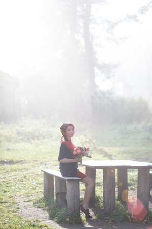 Girl in the image of a forest fairy with flowers in her hands. Sun rays beating down on woman walking in forestの写真素材