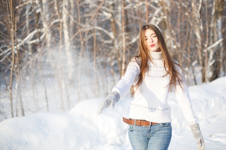 Woman throwing snowball. Flying Snowflakes. Sunny day. Joyful Beauty young woman Having Fun in Winter Park.の写真素材