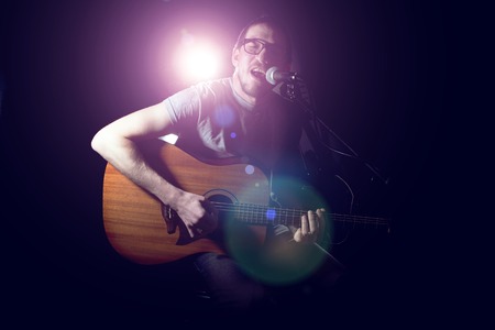 Musician playing acoustic guitar and singing on dark backgroundの写真素材