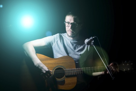 Musician playing acoustic guitar and singing on dark backgroundの写真素材
