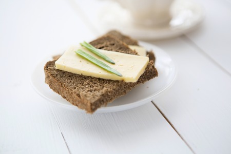 Dark bread slice with cheese and fresh onion on white wooden tableの写真素材