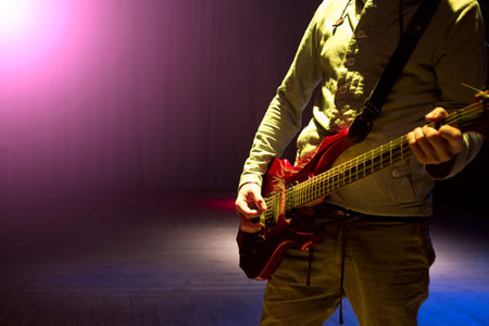 Young man playing on electric guitar on dark background