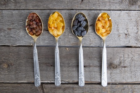 Raisins in metal spoons on wooden tableの写真素材