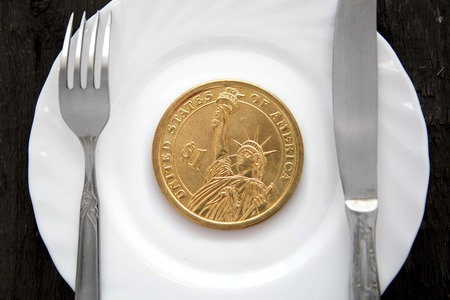 One dollar coin on a white plate next to fork and knifeの写真素材