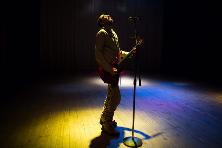 Man singer in plays guitar and sings on dark background
