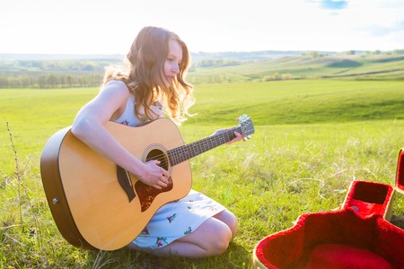 Beautiful young girl playing guitar in the field. Lens flare, selective focus, toned image.の写真素材
