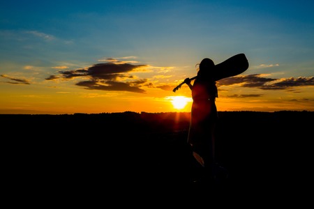 Silhouette woman playing guitar in the sunsetの写真素材