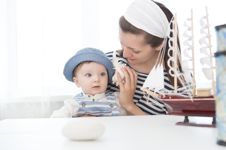 Mother and her baby boy listening sounds of the sea in a seashell. Mother and son in sea clothes, and sailors.の写真素材