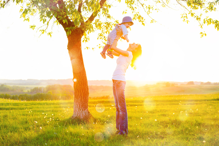Beautiful young woman with boy on the daisy meadow on a sunny day. Happy family on summer sunset. Mum with baby.の写真素材