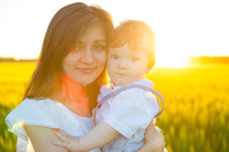 Baby and mother on nature in the park. Happy mother holding baby smiling on a wheat field in sunlight. Family happiness concept.の写真素材