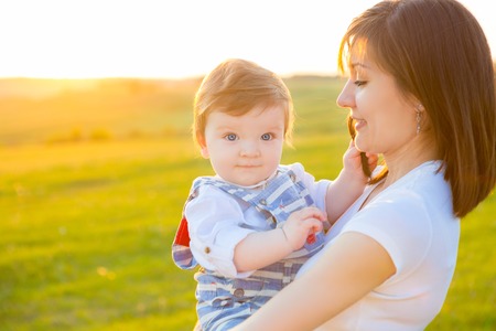 Beautiful young woman with baby boy on the meadow on the summer sunset. Happy family in the park. Outdoors. Mother with children.の写真素材