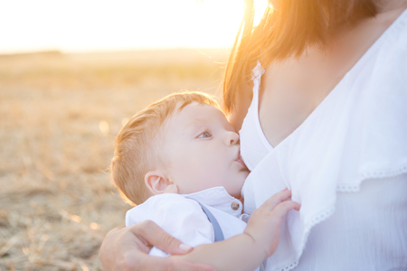 Mom is nursing her child in nature. Happy family sitting on the sunset background.の写真素材