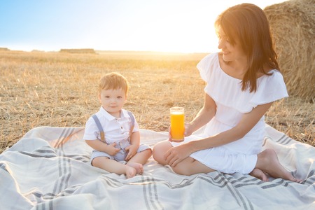 Mother and her son on holiday at a picnic. Mom is holding orange juice. Happy family relaxing in nature.の写真素材