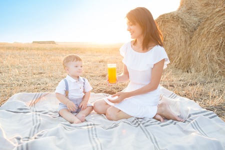 Mother and her son on holiday at a picnic. Mom is drinking orange juice. Happy family relaxing in nature. Healthy eating.の写真素材