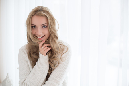 Portrait of beautiful blonde girl in pullover inside. The girl sits in an armchair and looking at the cameraの写真素材