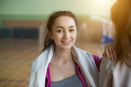 Two smiling women sitting on the wooden floor and relaxing after class in the gymの写真素材