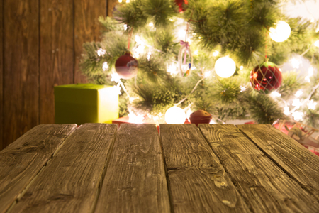 Blurred background of xmas tree lights, gifts and wall with wooden table of brown color. Christmas background.の写真素材