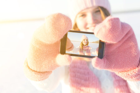 Pretty young female tourist takes selfie in winter. Beauty girl in hat and scarf.